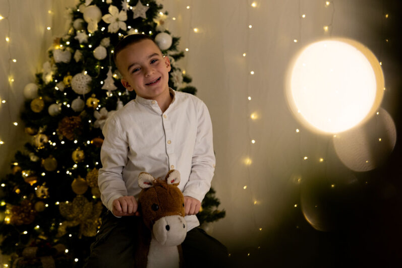 Bambino con sfondo un albero di Natale durante un set fotografico
