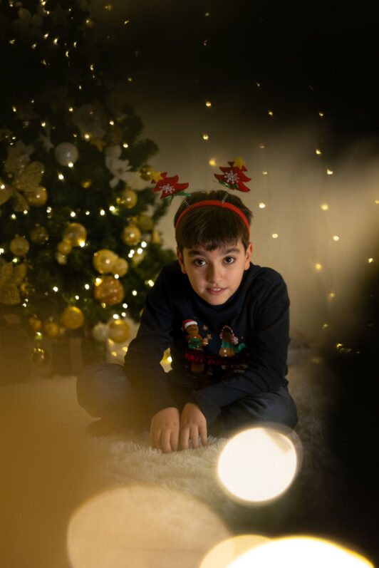 bambino a sedere a fianco ad un albero di Natale