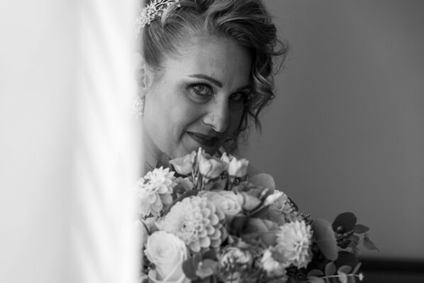 La sposa fa capolino da dietro la tenda coprendosi un pò il viso con il bouquet di fiori